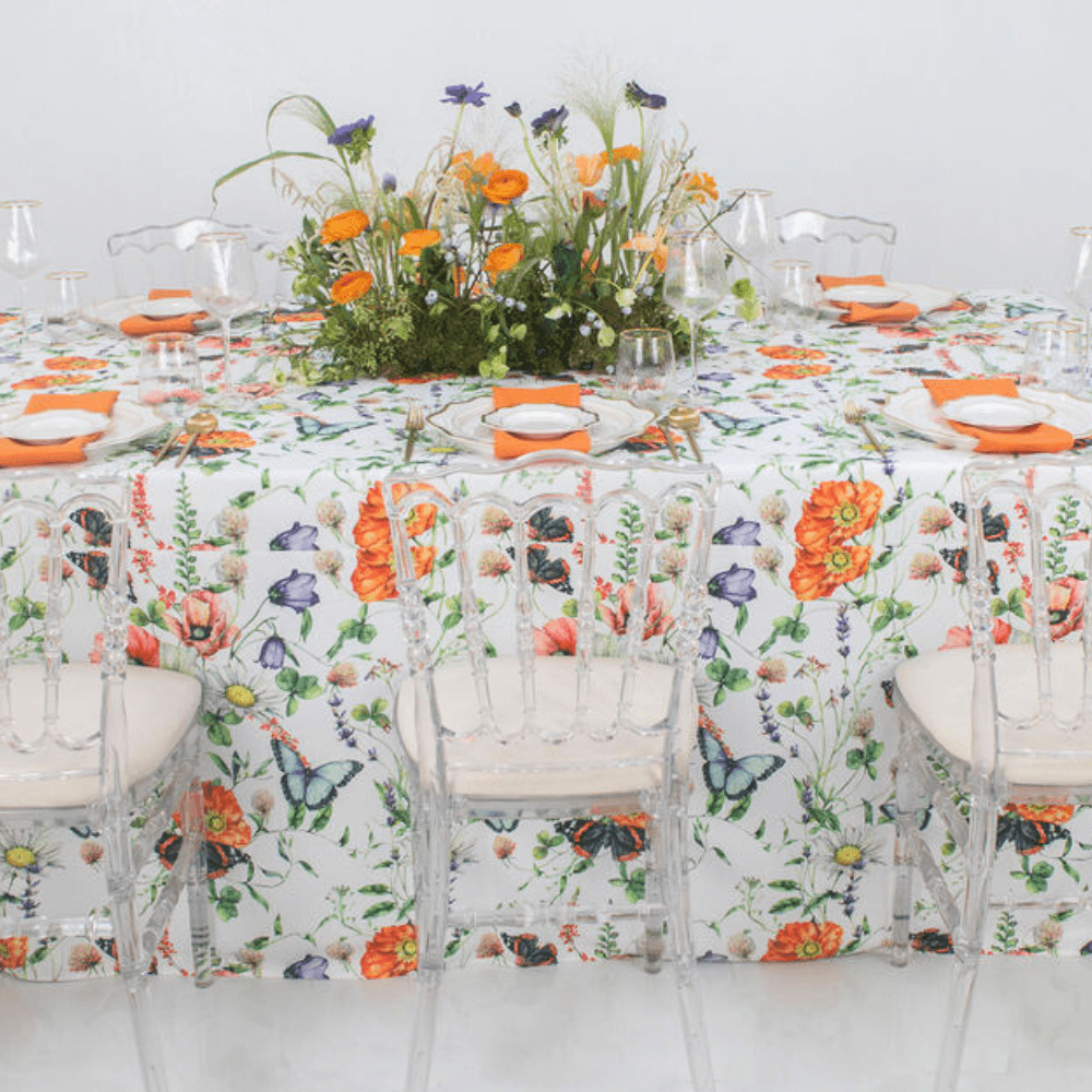 Butterfly Meadows- Dining Setup featuring a table with a floral centerpiece, acrylic chairs, charger plates, gold cutlery, wine glasses, and napkins for eight guests.