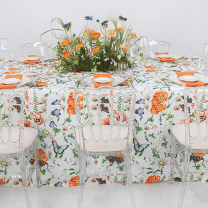 Butterfly Meadows- Dining Setup featuring a table with a floral centerpiece, acrylic chairs, charger plates, gold cutlery, wine glasses, and napkins for eight guests.