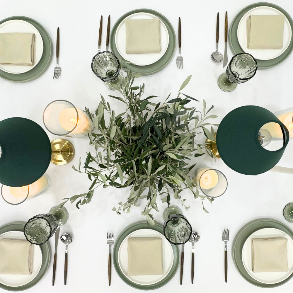 Serene Green- Dining Setup: Elegant table arrangement for eight with plates, wooden cutlery, goblets, napkins, and chairs, enhanced by green lamps and a floral centerpiece.