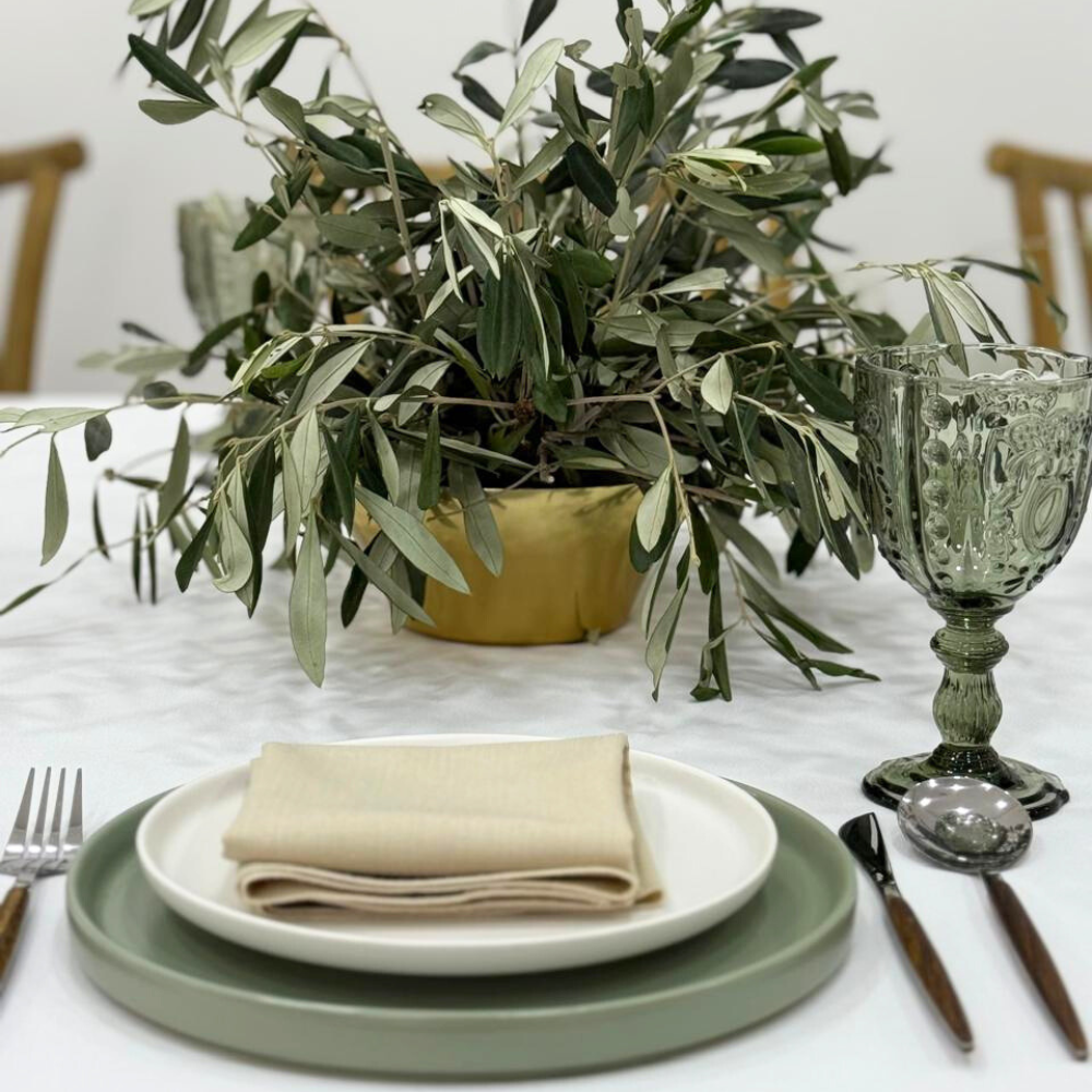 Serene Green- Dining Setup with a table displaying a plant, a plate with folded napkins, and a close-up of glassware and silverware.