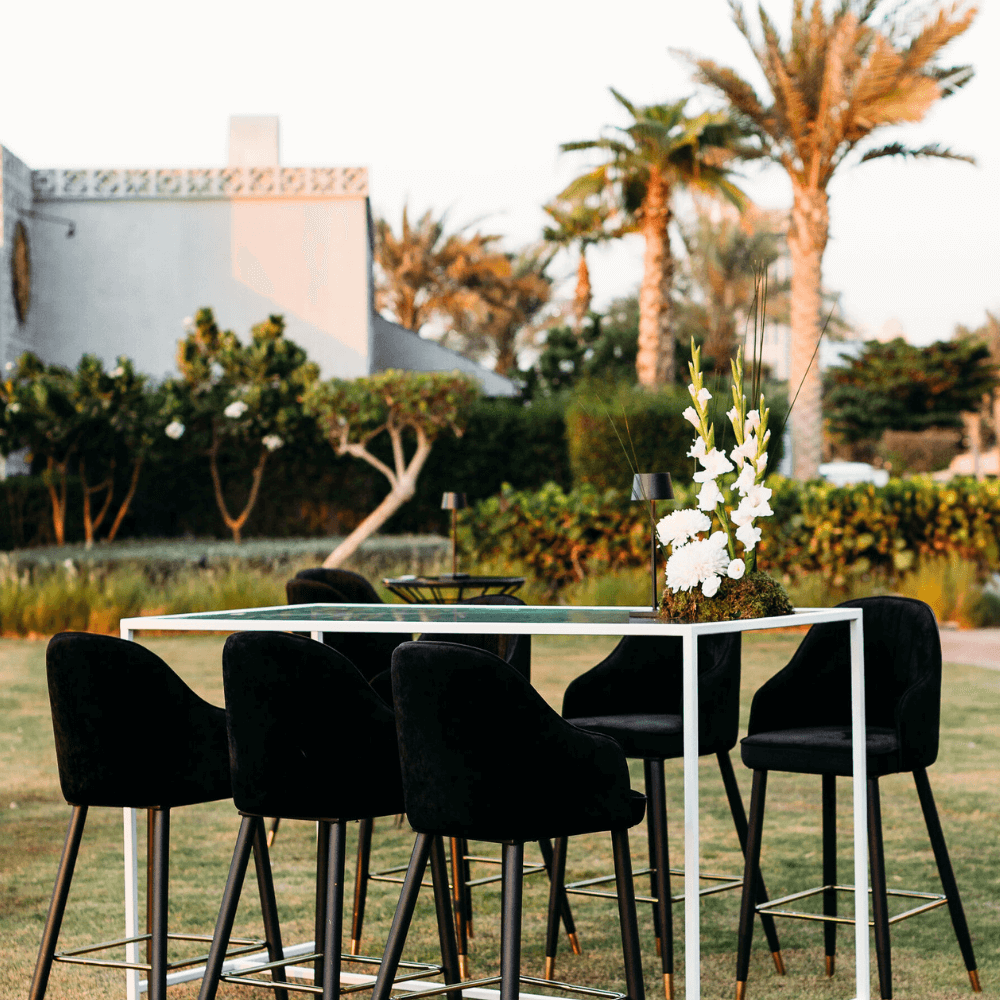 Monochromatic Cocktail Setup: Outdoor table with eight stools and a flower centerpiece, designed for hosting eight guests in a grassy setting.
