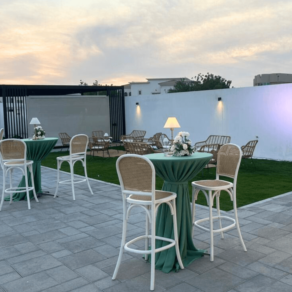 Sage Twilight-Cocktail Setup featuring a table, eight stools, a floral centerpiece, and a wireless lamp on a patio.