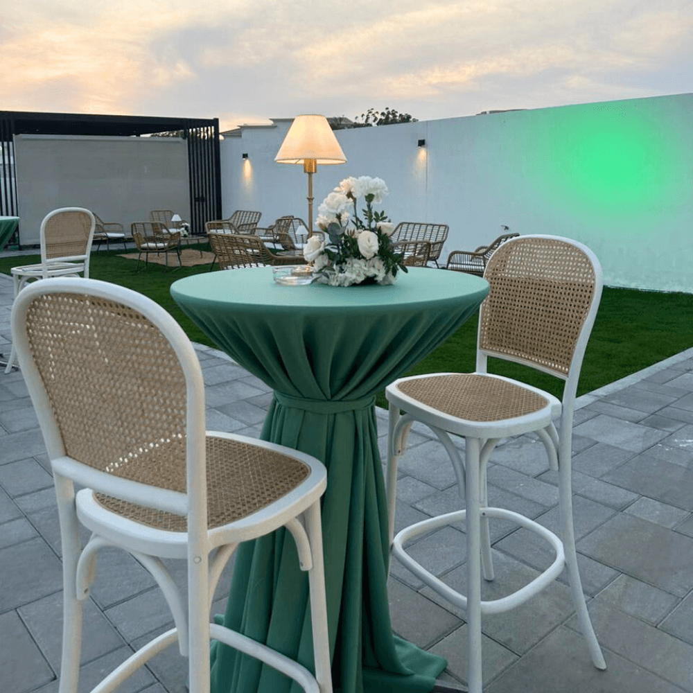Sage Twilight-Cocktail Setup featuring a table for 8 with stools, flower centerpiece, and wireless lamp on a patio, ideal for events.