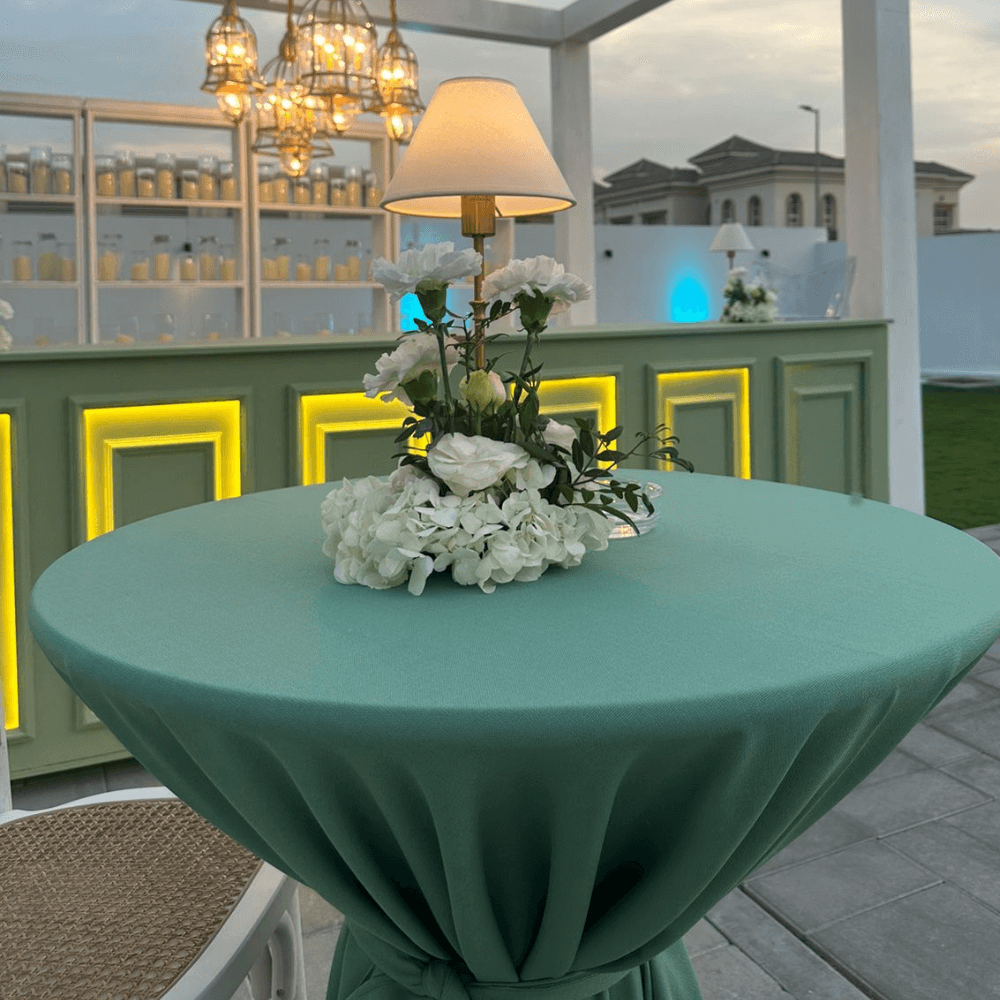 Sage Twilight- Cocktail Setup: Table with floral centerpiece, wireless lamp, and seating for eight, ideal for party and event settings.