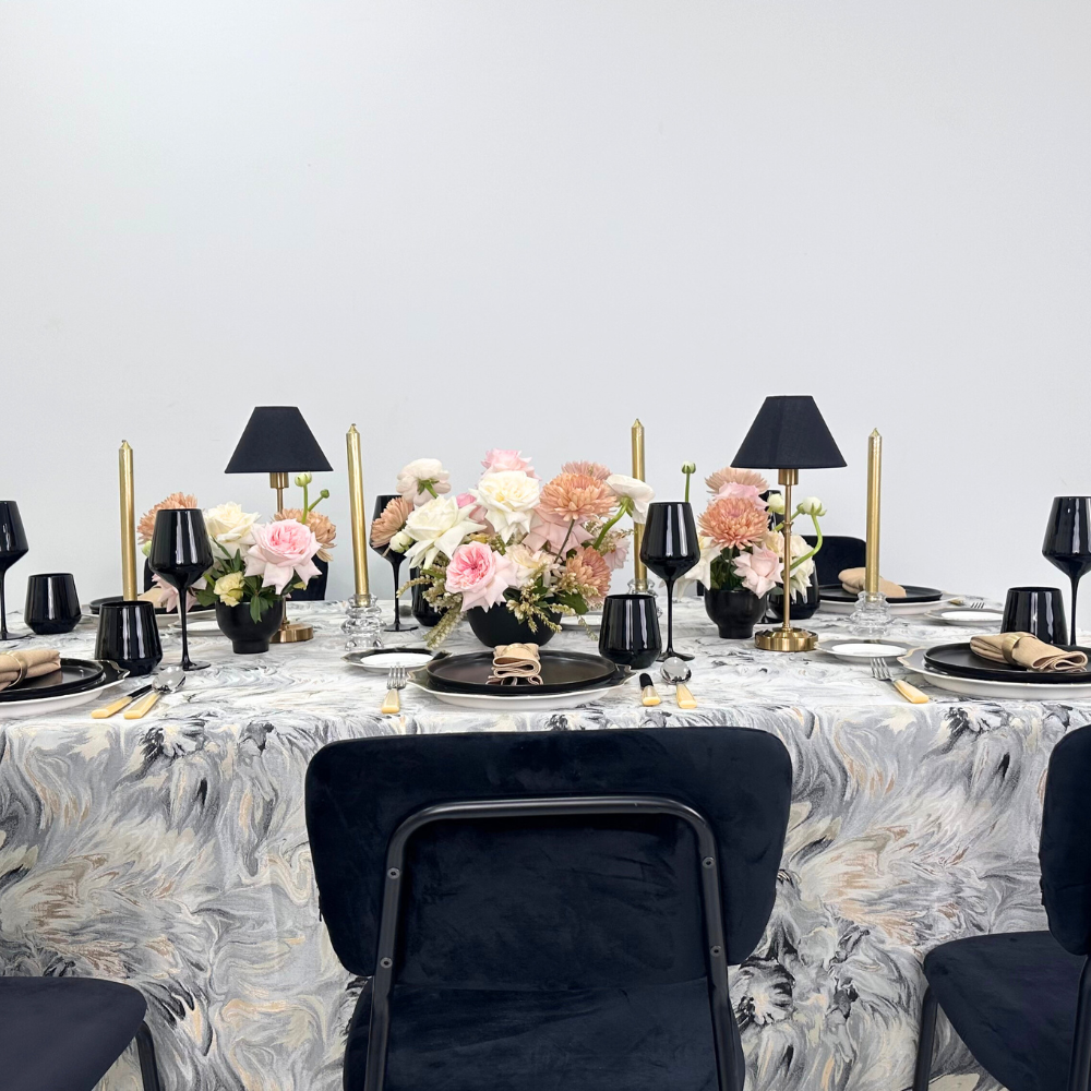 Opulent Twilight-Dining Setup featuring a table set for eight with black chairs, flower centerpieces, and elegant tableware, ideal for upscale events.