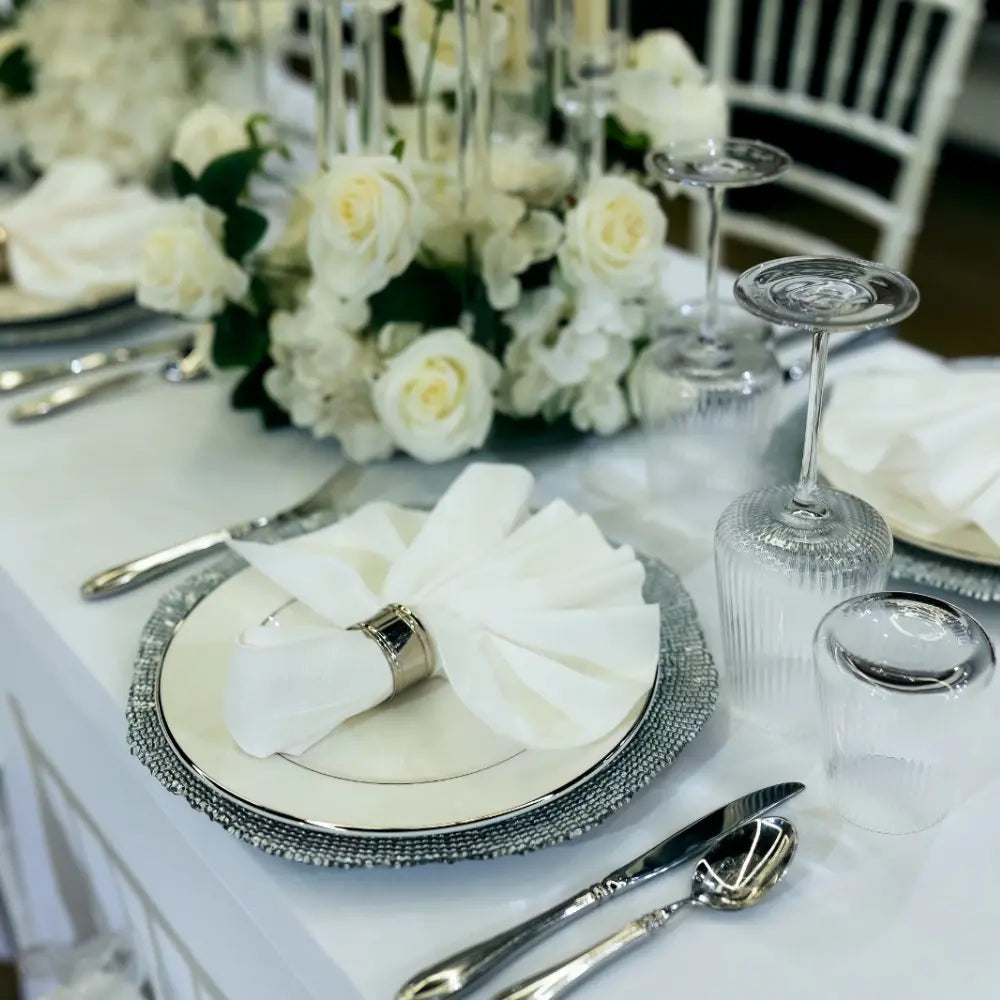 CHARGER PLATE - SILVER GRAIN elegantly enhances a formal table setting with a white dinner plate, silverware, and floral centerpiece at an upscale event.