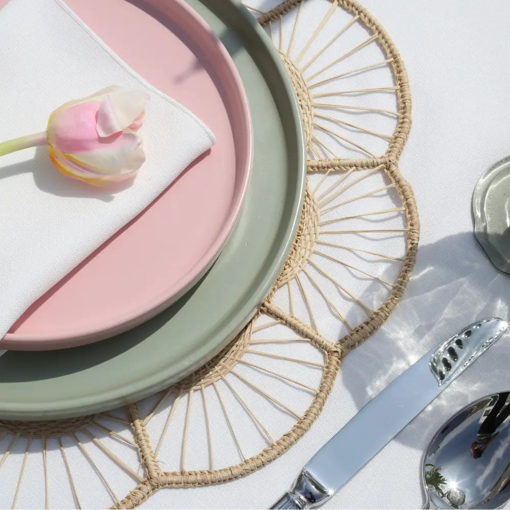 Overhead view of a table setting featuring the CHARGER PLATE - FLORAL RATTAN WIRE, highlighting its sunburst pattern with elegant ceramic plates and silverware.