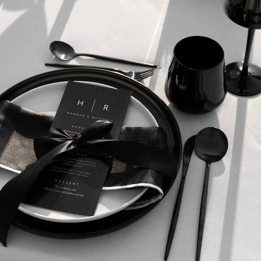 CERAMIC PLATES - BLACK, elegantly set on a white tablecloth, featuring black charger and dinner plates with matching black cutlery and glassware, perfect for formal events.