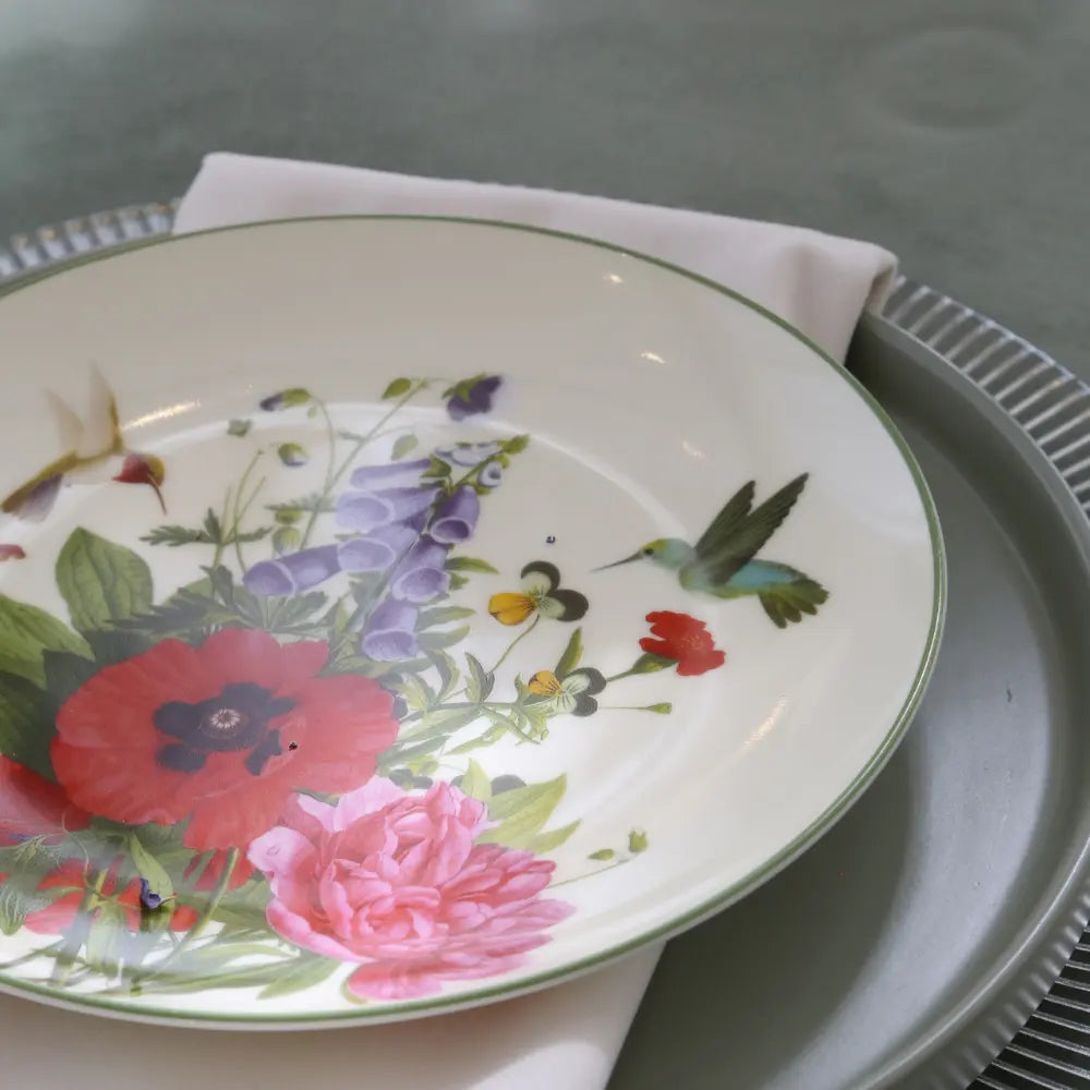 VINTAGE FLORAL PLATES: Decorative china plate with red and pink blossoms, hummingbird motif, on a white napkin and silver-toned charger. Perfect for elegant table settings.