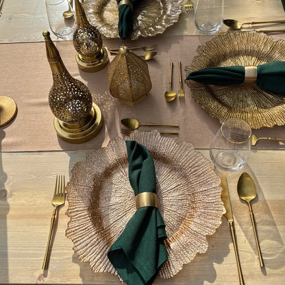 Gold starburst charger plate elevates table setting with forest-green napkin, matte-gold flatware, and ornate brass lanterns, creating an elegant, sophisticated dining experience.