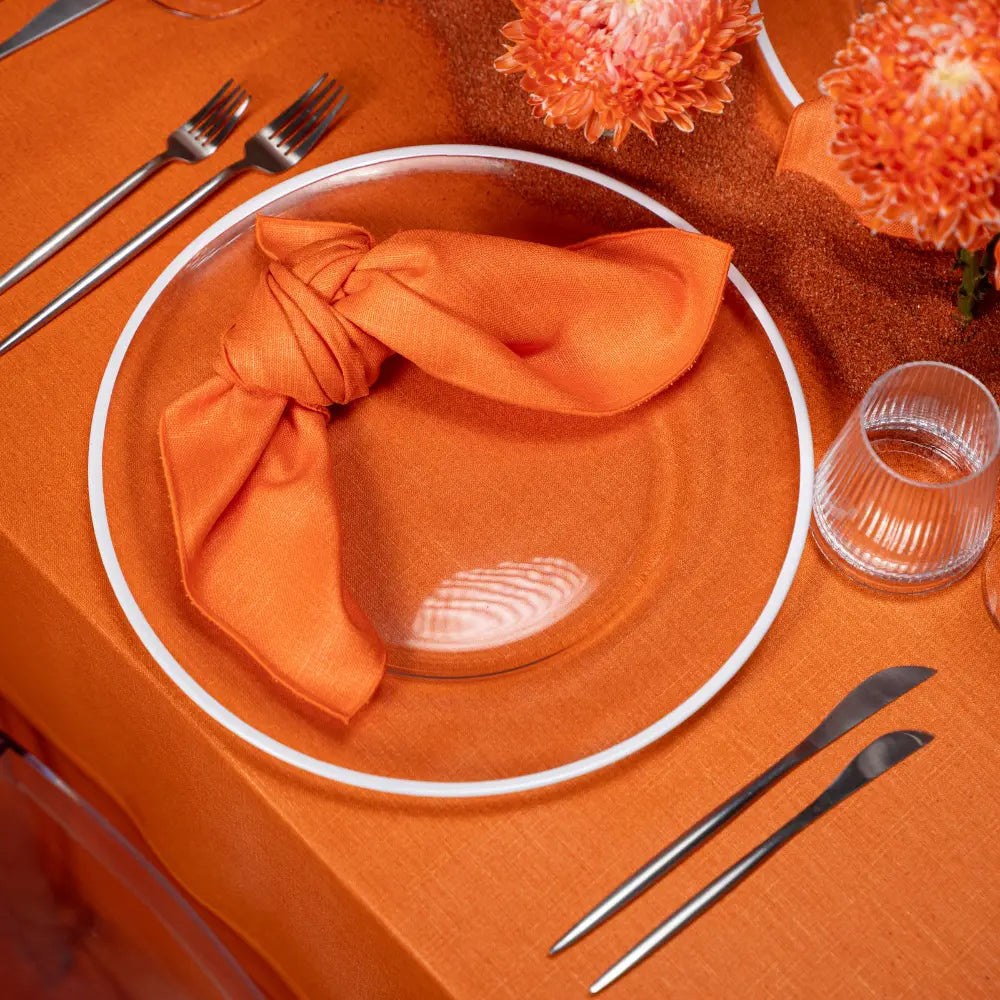 Modern Silver Cutlery set on an orange-themed table with glass plate, knotted napkin, and chrysanthemum accents, showcasing minimalist elegance for events.