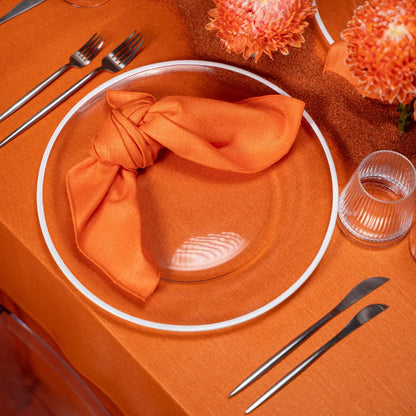 Modern Silver Cutlery set on an orange-themed table with glass plate, knotted napkin, and chrysanthemum accents, showcasing minimalist elegance for events.