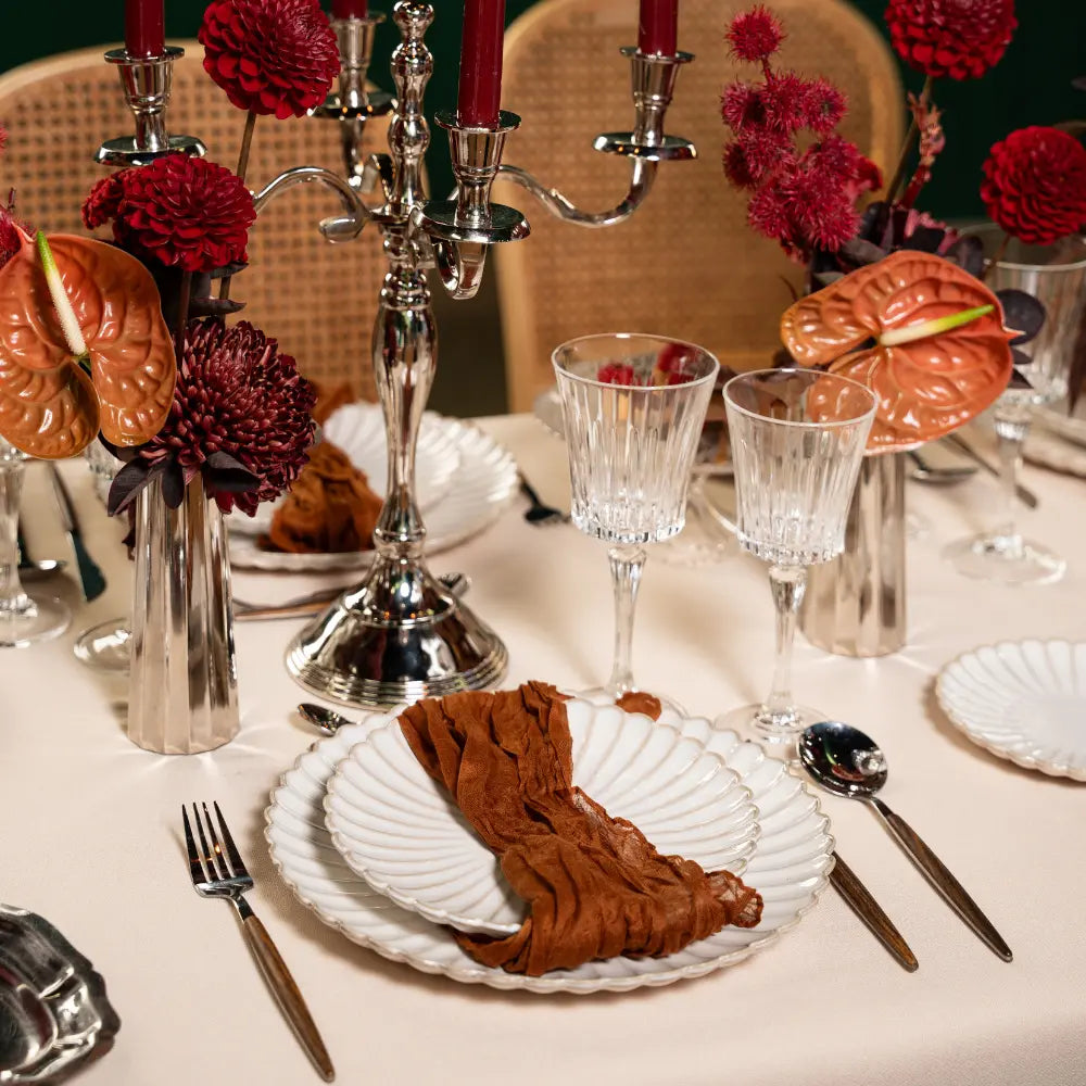 Scalloped Like Plates elegantly set on a neutral tablecloth, accented by rust napkins, polished flatware, crystal glasses, and rich red blooms, creating a sophisticated dining scene.