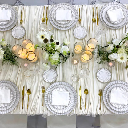 SCALLOPED LIKE PLATES elegantly layered on a formal banquet table with gold-tone flatware, clear glasses, ivory candles, and white-green floral arrangements.