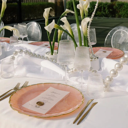 CHARGER PLATE - PINK PEARL W/ GOLD RIM elegantly set with gold flatware and ribbed goblets, creating a sophisticated table setting for upscale events.