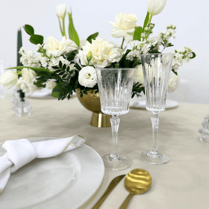 Sand Elegance-Dining Setup showing a flower centerpiece, glasses, napkins, and gold cutlery arranged on a table for an elegant event setting.
