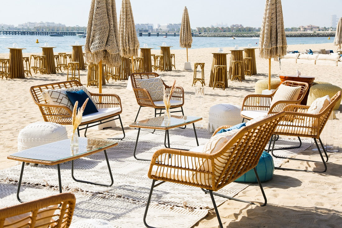 RATTAN COFFEE TABLE W/ GLASS TOP set on a beach, surrounded by chairs, ideal for outdoor events and gatherings.