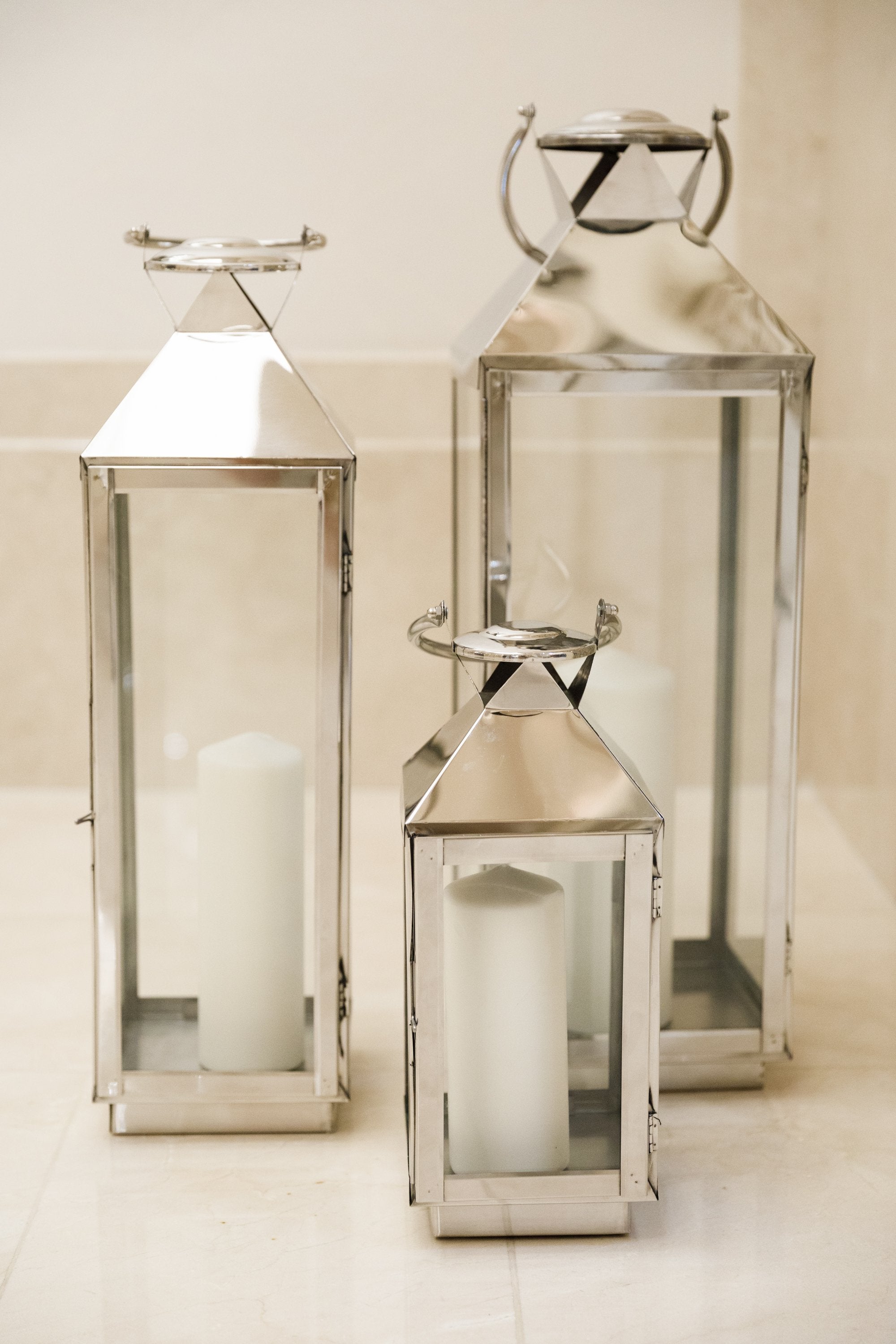 Silver lanterns in large, medium, and small sizes, each with a glass case for candles, ideal for enhancing event decor. Candles not included.