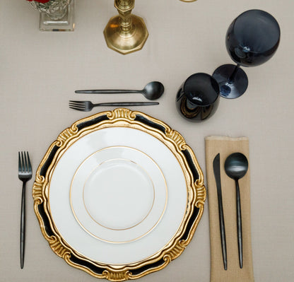 Modern black cutlery on a table, styled with a gold-rimmed plate and silverware, ideal for enhancing dinner party aesthetics.