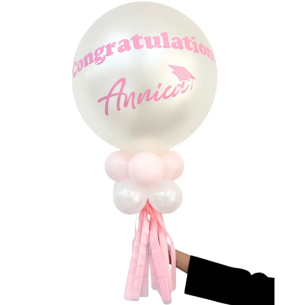 Personalized Balloon Wand with Congratulations Annica on a pearl-white balloon, surrounded by pink and white mini-balloons, held by a hand.
