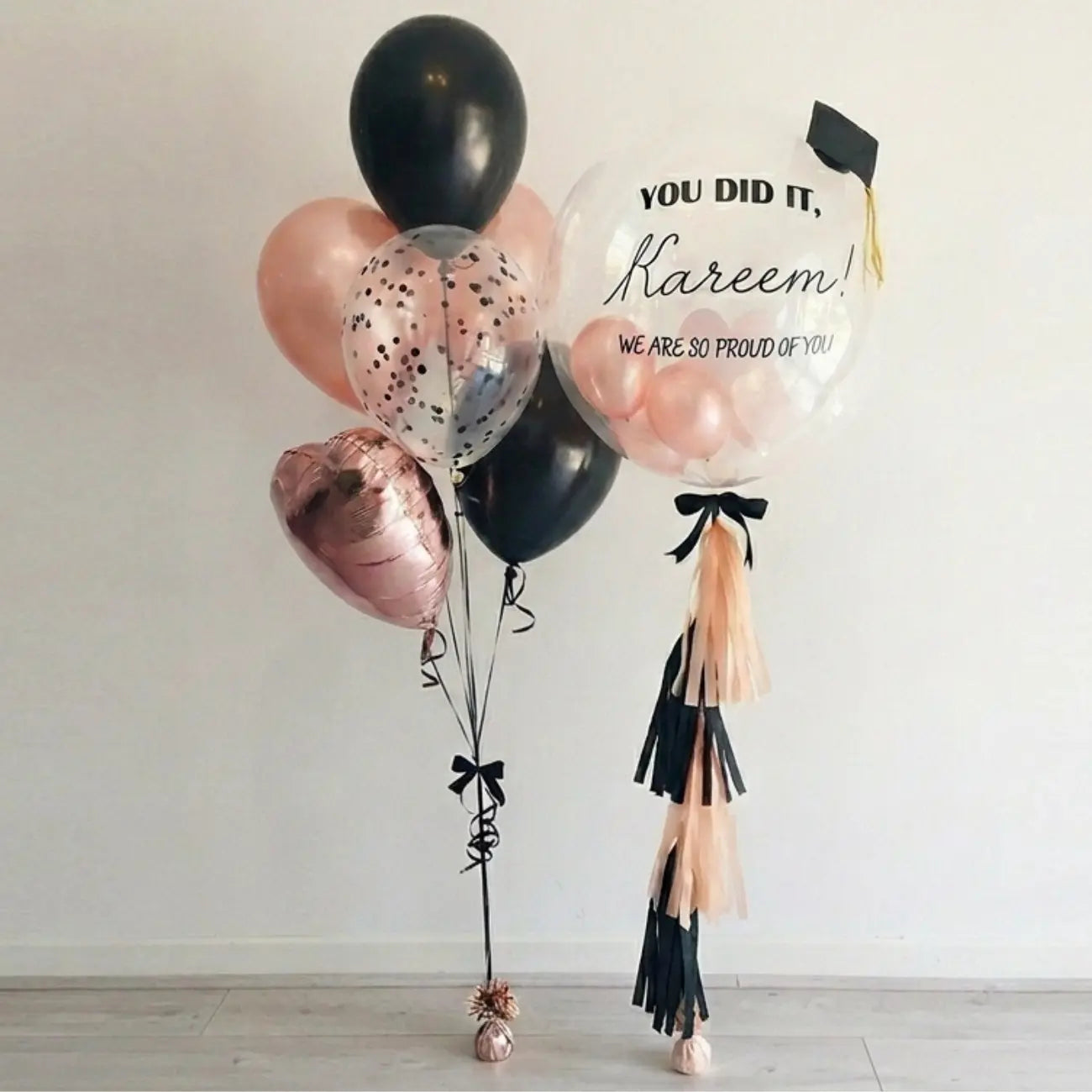 Blush Rose Bliss Balloon Bouquet featuring a black and rose-gold theme with confetti-filled balloons and a personalized congratulatory message, perfect for elegant graduation celebrations.