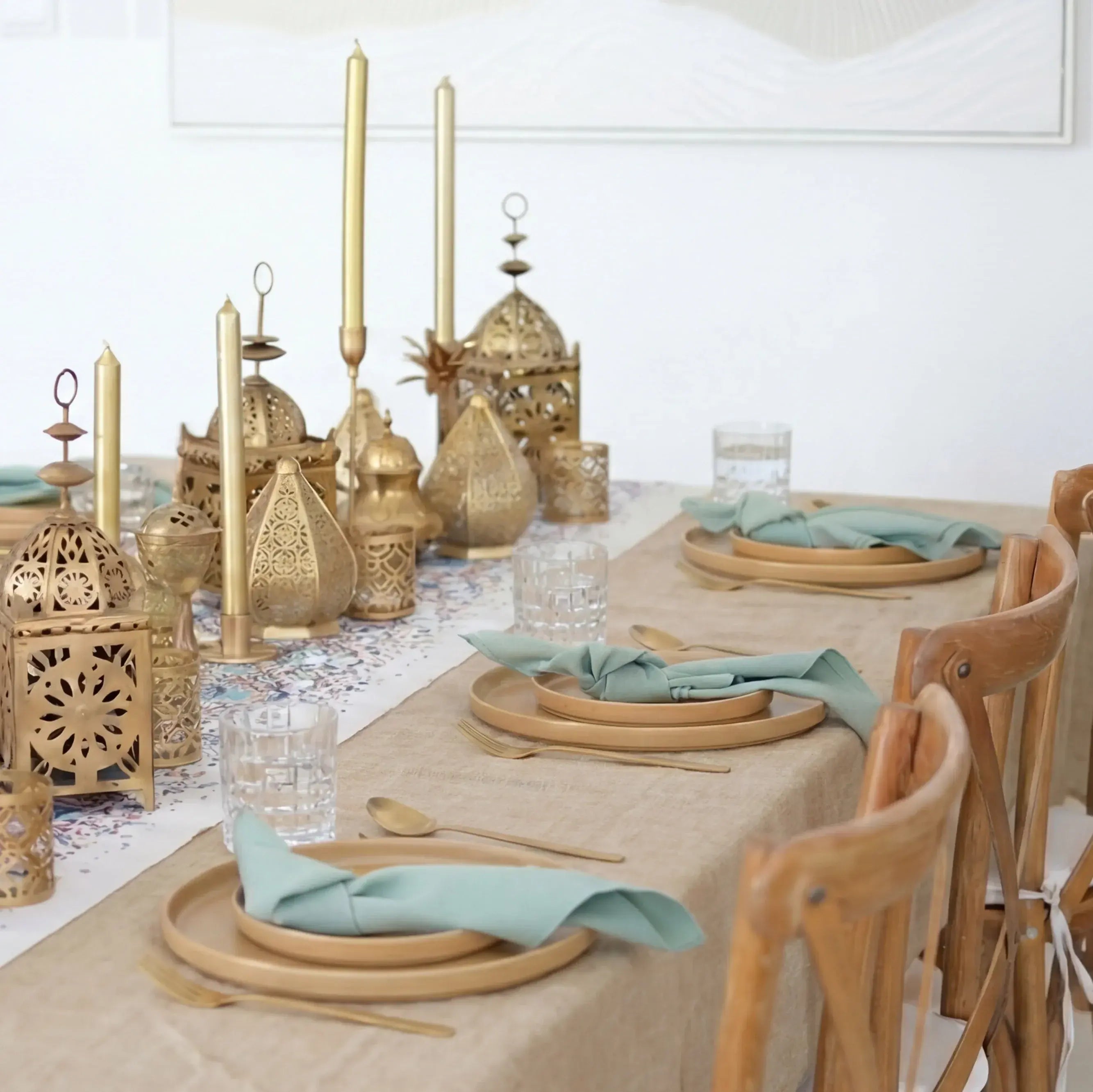 Decorative table setting with gold lanterns, candles, and green napkins on a white tablecloth.