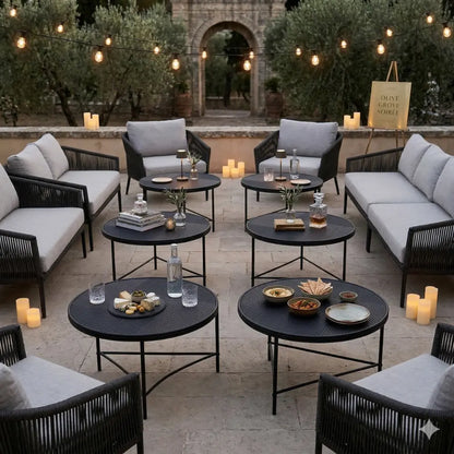 BLACK LINED COFFEE TABLE surrounded by sofas on a stone patio at an olive grove soirée, adorned with snacks, drinks, and glowing lights for an event atmosphere.