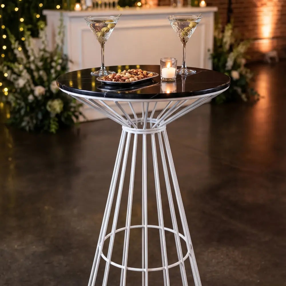 WHITE WIRE COCKTAIL TABLE-BLACK MARBLE TOP with martini glasses, nuts, and candle, ideal for elegant gatherings or events, showcasing modern, versatile design.