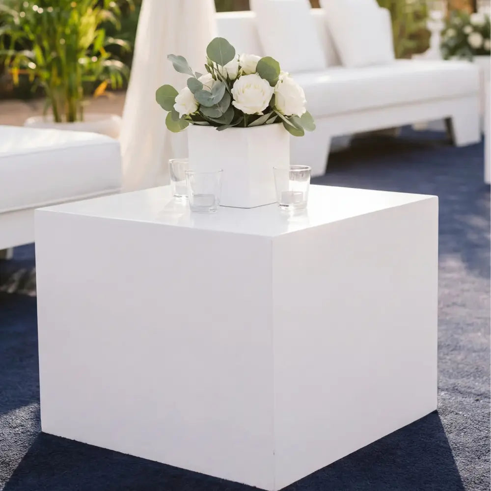 BOXY WHITE COFFEE TABLE in a minimalist outdoor setup, featuring a white planter with flowers and eucalyptus leaves, flanked by glass votive holders.