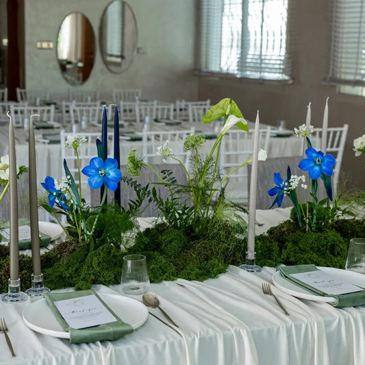 Classic Baby Shower Dinner Setup featuring an elegant tablescape with lush greenery, cobalt-blue flowers, white charger plates, and taper candles, perfect for celebratory gatherings.