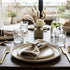 Dining table set with plates, cutlery, glasses, and bread on a wooden table.