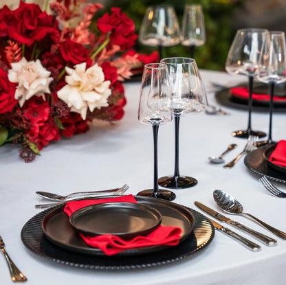 Black Stem Glassware Collection with matte black stems and clear bowls on an elegantly set table with black plates and red napkins for stylish events.