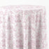 A round table covered with a white tablecloth featuring a light pink classic toile de Jouy pattern with figures, trees, and classical architecture.