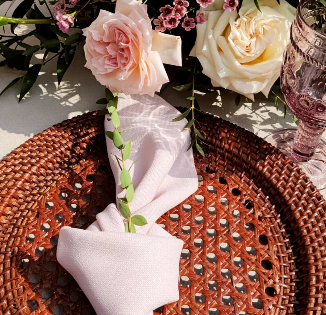 Rattan charger plate on a table, adorned with a folded napkin and floral centerpiece, perfect for rustic or boho-themed events.