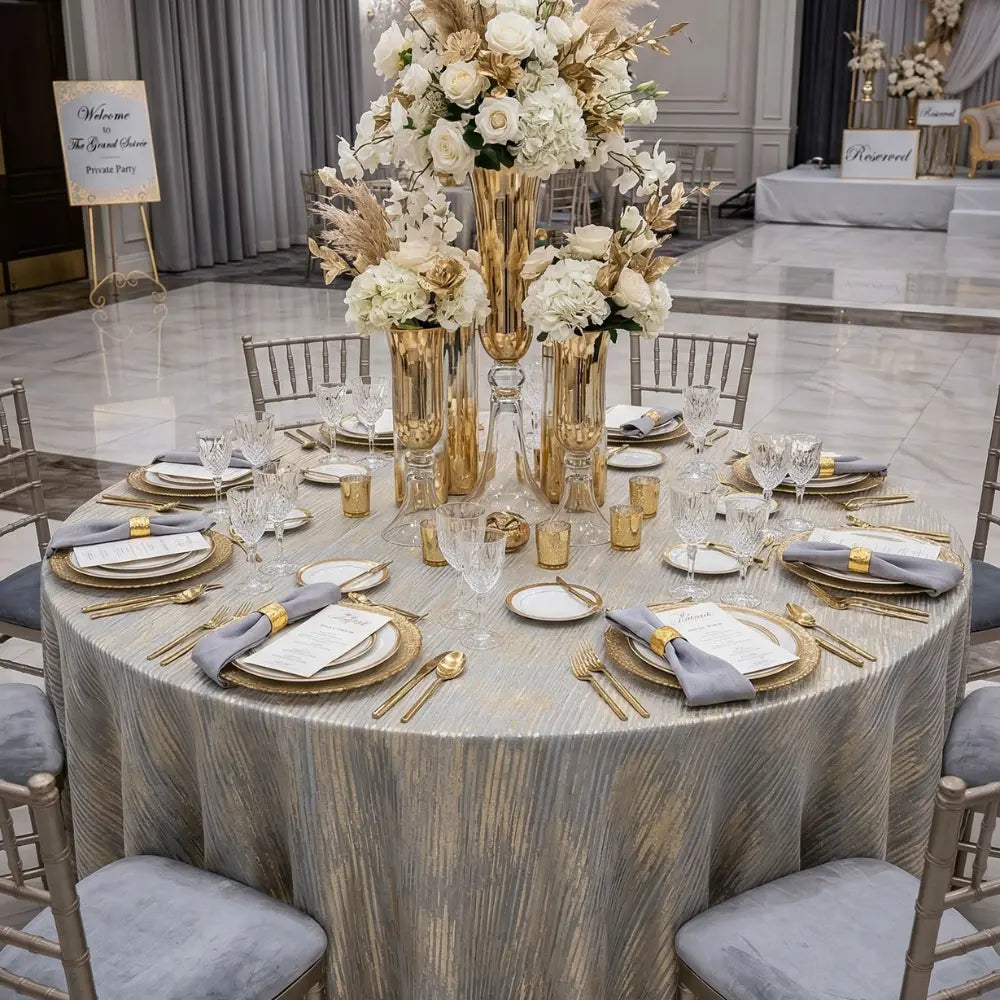 CELESTIAL HORIZON ROUND TABLECLOTH adorns an elegant round table set for a formal event, with gold accents, crystal glassware, and floral centerpieces.