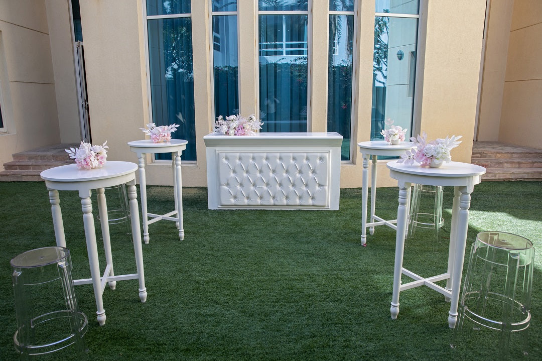 White Wood Cocktail Table on a green lawn, surrounded by chairs, ideal for versatile event settings from Party Social&