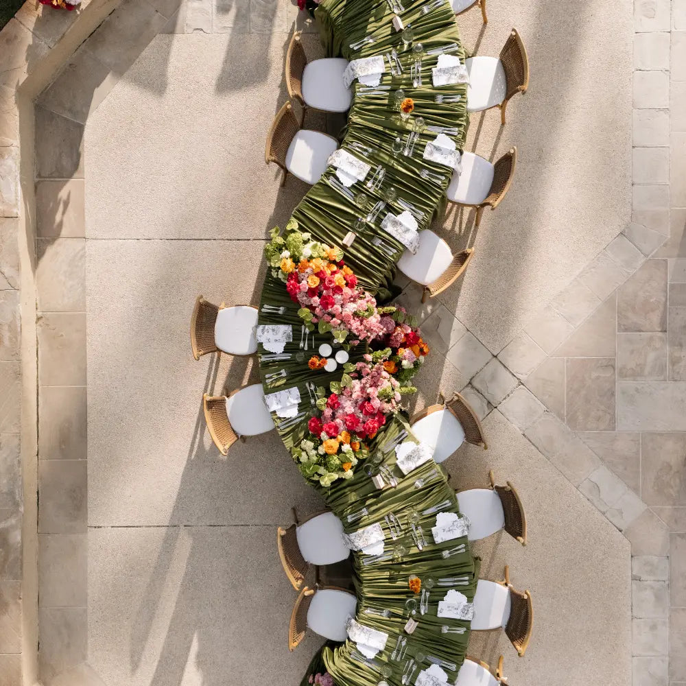 White Crescent Dining Table with curved design set for an elegant outdoor event, featuring lush floral arrangements and classic woven-back chairs.