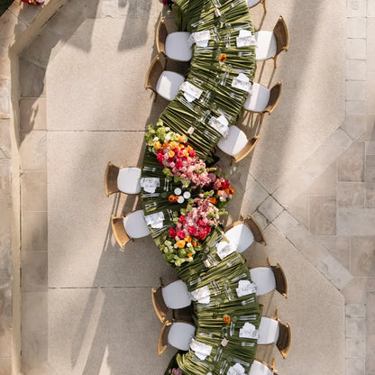 White Crescent Dining Table with curved design set for an elegant outdoor event, featuring lush floral arrangements and classic woven-back chairs.