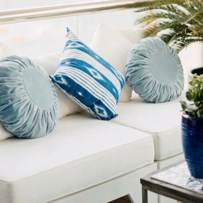 CUSHION COVER ROUND VELVET atop a light sofa with decorative pillows, offering a bold, luxurious touch for any event setting.