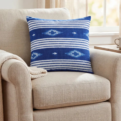 CUSHION NAVY/WHITE NAUTICAL on an armchair in a cozy nook, featuring a bold blue and white striped pattern with ikat-style design.