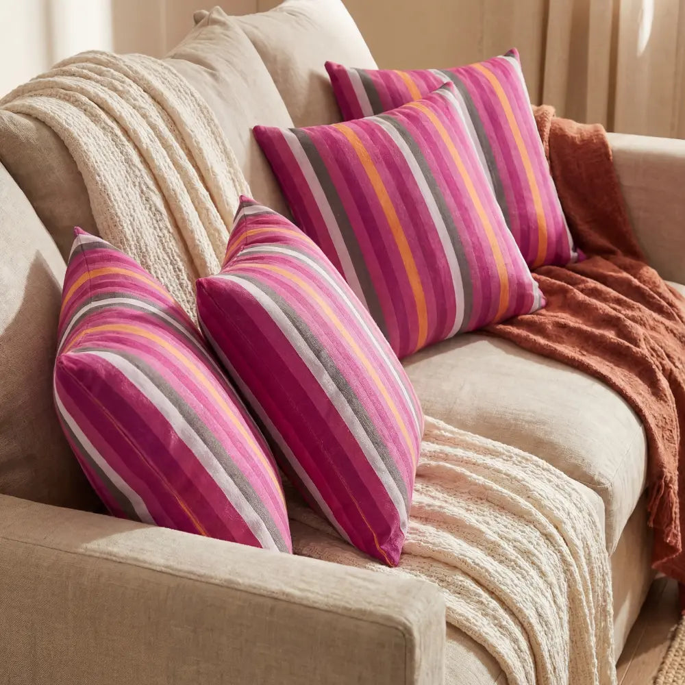 CUSHION PINK LINED PRINT VELVET on a neutral sofa, featuring vibrant pink and multicolor stripes, adding a lively touch to event-ready seating arrangements.