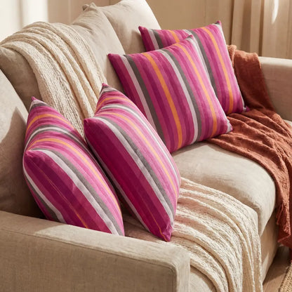 CUSHION PINK LINED PRINT VELVET on a neutral sofa, featuring vibrant pink and multicolor stripes, adding a lively touch to event-ready seating arrangements.