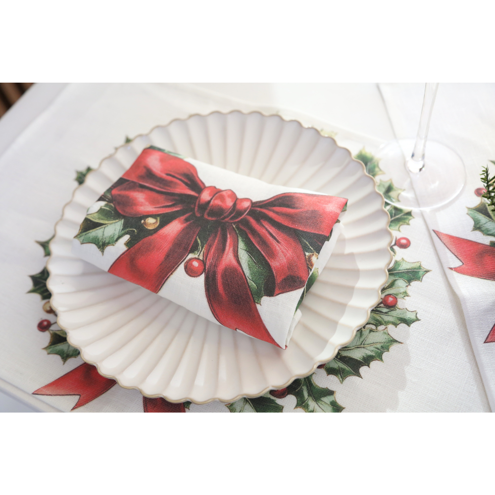 Evergreen Knot Linen Napkin on a scalloped plate, featuring a festive holly-and-ribbon design, part of a luxurious holiday table setting from Party Social.