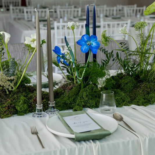 Classic Baby Shower Dinner Setup featuring elegant white china, metallic cutlery, green napkin, lush greenery centerpiece with blue accents, and chic taper candles.