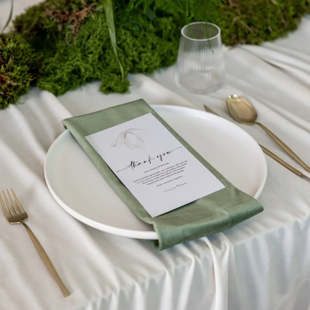 Classic Baby Shower Dinner Setup featuring a formal place setting with gold-tone cutlery, sage napkin on white plate, and greenery, creating a minimalist, elegant atmosphere.