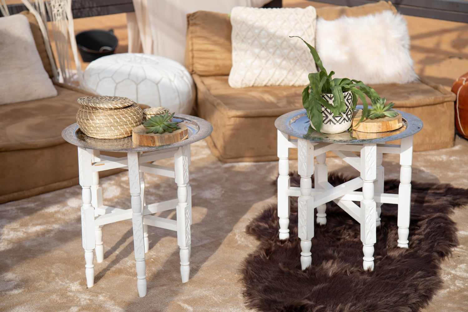 Moroccan folding tables with silver and gold platters, ideal for events. Featured among plants and decor, perfect for parties or social gatherings.