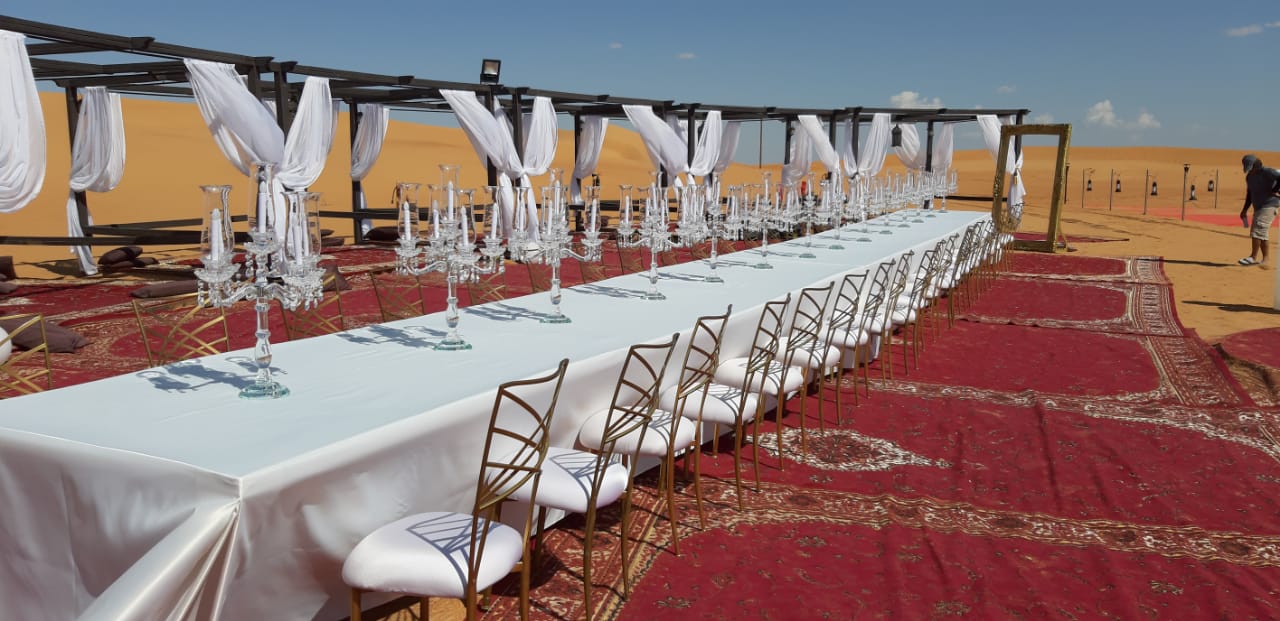 Crystal glass candelabra on a long table with white tablecloth and candlesticks, ideal for elegant party settings.