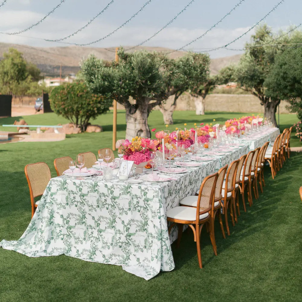 Long table set for a meal outdoors with floral arrangements and greenery.