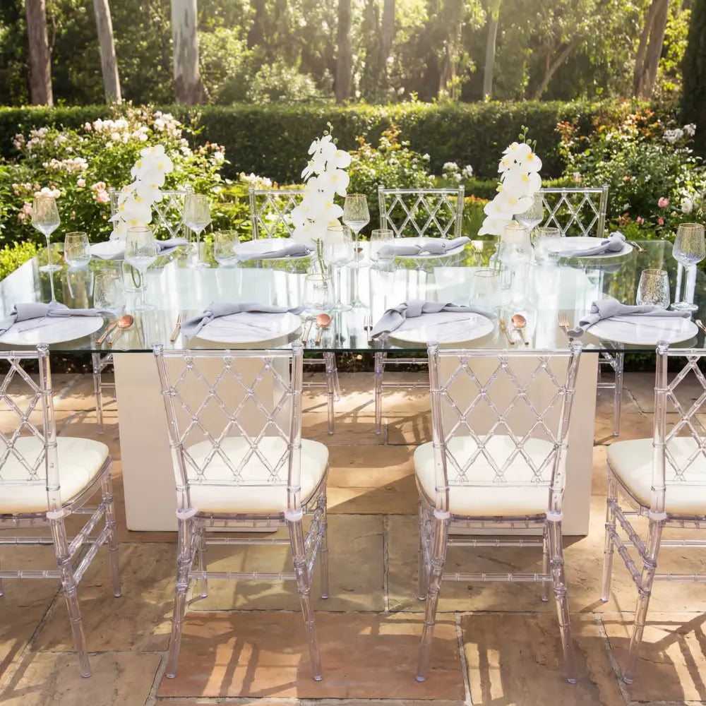 DIAMOND BACK ACRYLIC CHAIR elegantly surrounds a glass dining table set for an upscale event, showcasing its modern geometric design in a garden setting.