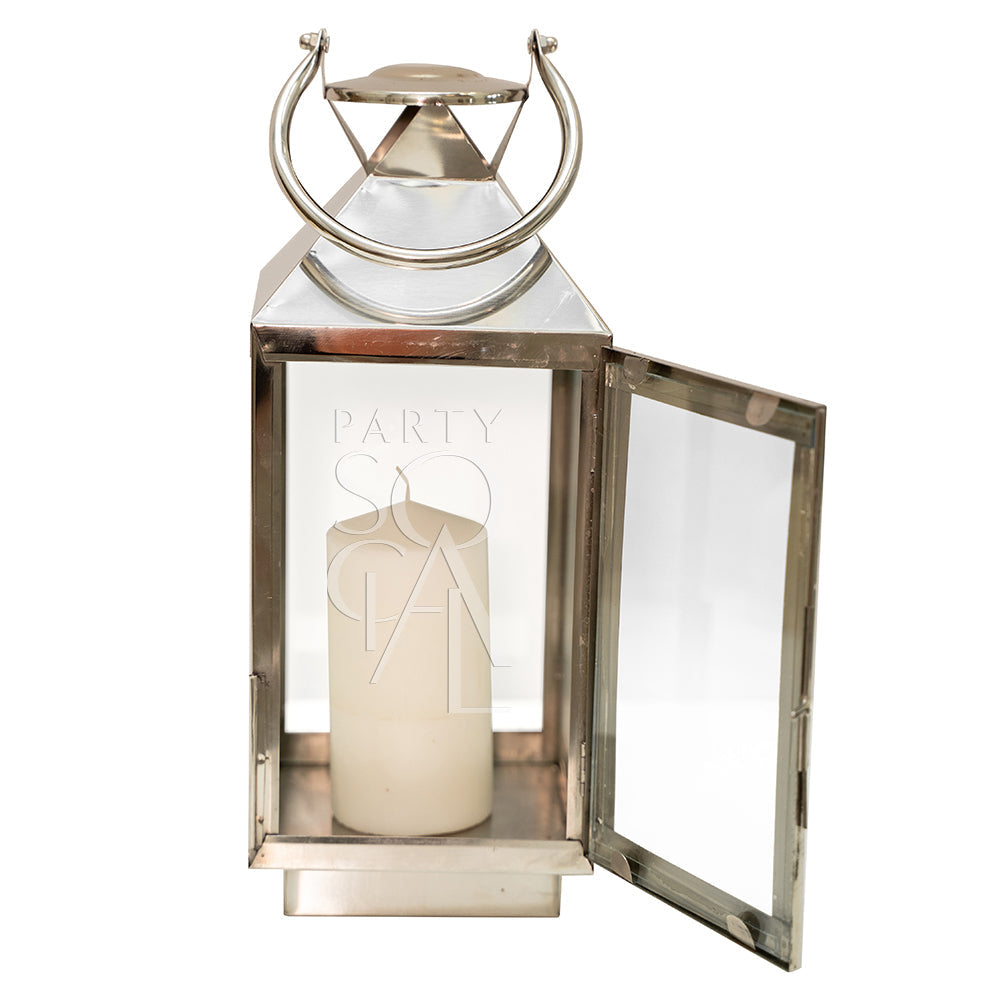 Silver lantern with a lit candle inside, showcasing intricate metalwork. Part of Party Social&